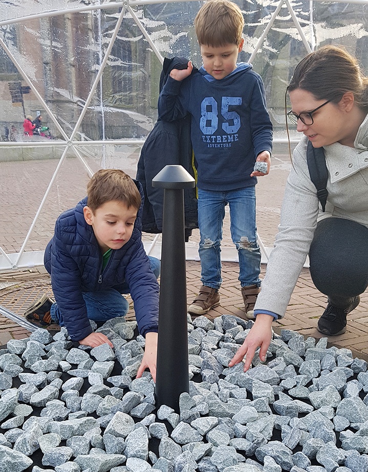 Een jong gezin legt stenen bij het monument op het Canadaplein.