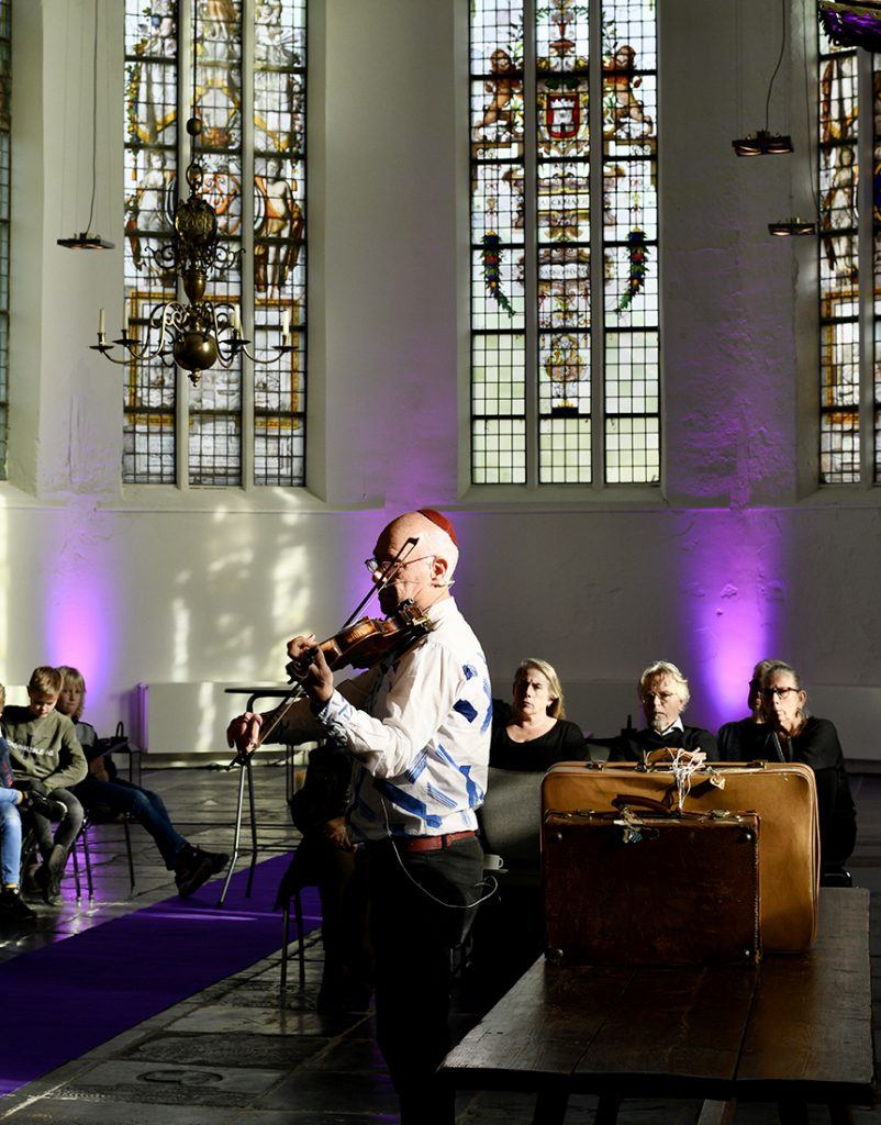 Robert Duizend vertelt het persoonlijke verhaal over het lot dat zijn ouders trof. Hij bespeelde daarbij zijn vaders viool in de Grote Kerk in Schermerhorn. Foto: Noa Duizend