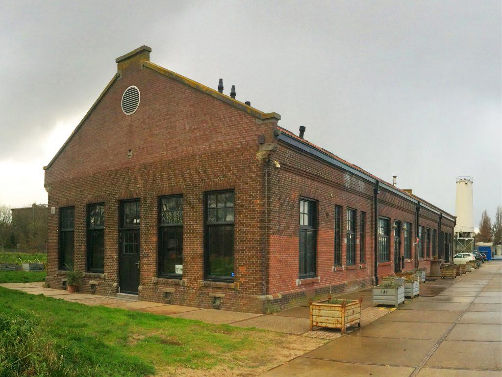 De Gasfabriek staat groot in het midden van de foto met links gras en rechts stoeptegels.