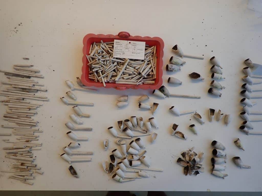 Pijpenkoppen en fragmenten van pijpenstelen uitgespreid op een tafelblad