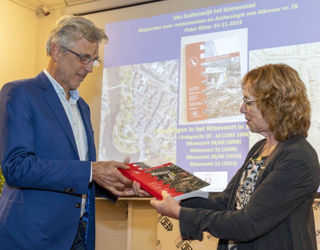 Wethouder Anjo van de Ven overhandigt het eerste exemplaar van RAMA 26 aan Bert de Raaf van de Alkenaer