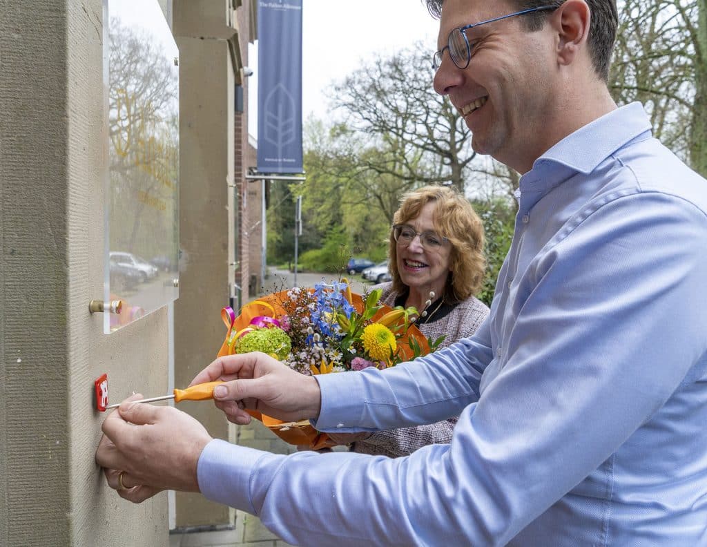 Wethouder Anjo van de Ven schoeft samen met Jerry Burg een emaille bordje op monument Schutterswei