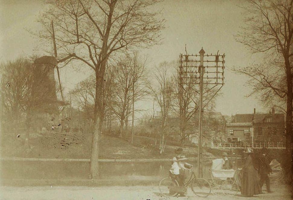 Molen van Piet op het bolwerk aan de Kennemersingel in 1912. Op de voorgrond een telefoonmast van Pot, een dame met fiets en twee echtparen met kinderwagens.