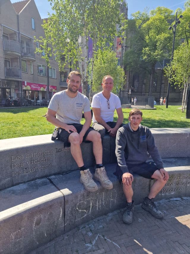 Het team van Swart Natuursteen op de stenen bank. Met links de eerste dichtregel: Les sanglots longs des violons de l 'automne (De lange snikken van de violen van de herfst)