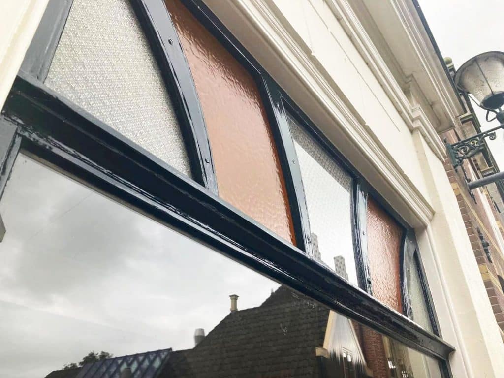 Het etalageraam is verfraaid met een bovenlicht van gekleurd en gegoten structuurglas.