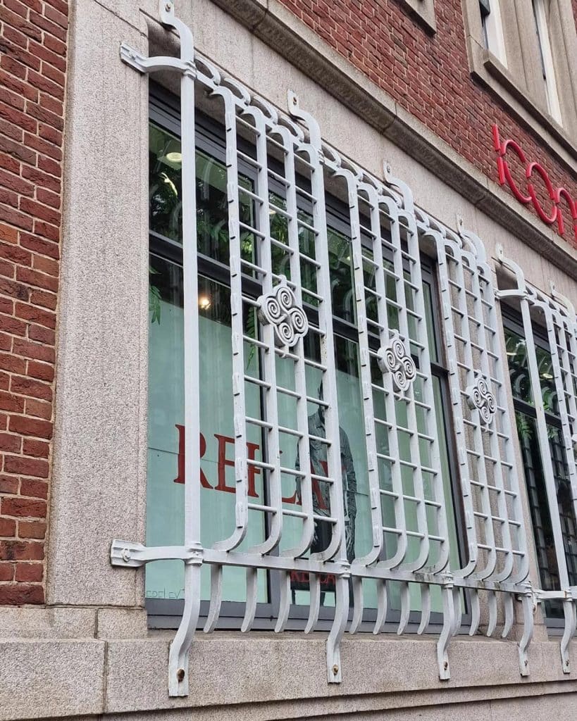 Sierlijke maar goed zichtbare smeedijzeren roosters voor de raamopeningen van De Nederlandsche Bank in Alkmaar.