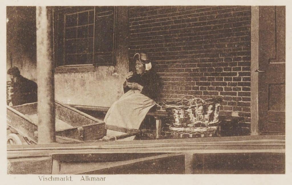 Een vissersvrouw in de galerij op een visbank. Circa 1921. Waar denk je dat de term viswijf vandaan komt? De vrouwen die hun vis op de markt verkochten schreeuwden hard om hun waar aan de man te brengen. Dat lawaai was hinderlijk en rijke stedelingen lieten dan ook hun dienstboden de boodschappen doen. Je begrijpt wel waarom in de nette straten zoals de Langestraat geen markt gehouden werd.