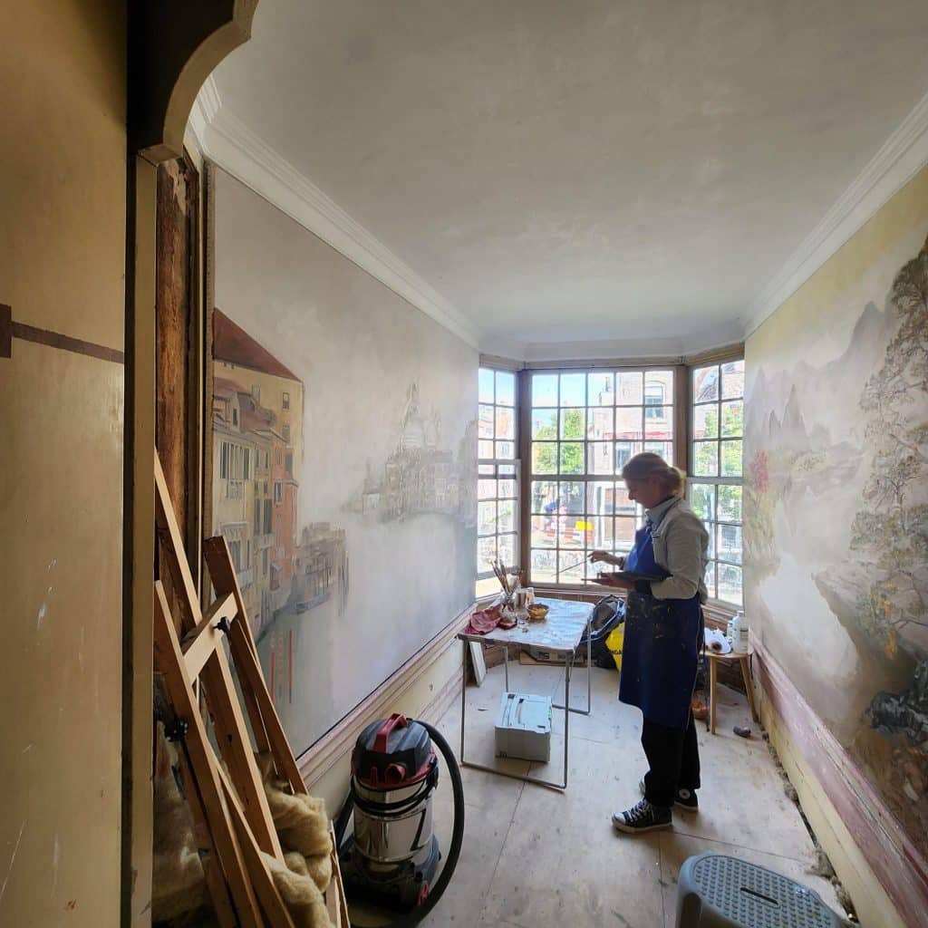De muren in de erkerkamer zijn bespannen met canvas in het Smalste Huisje aan het Luttik Oudorp. Deze worden beschilderd met een Venetiaans tafereel links en een berglandschap met bomen rechts. 2025.