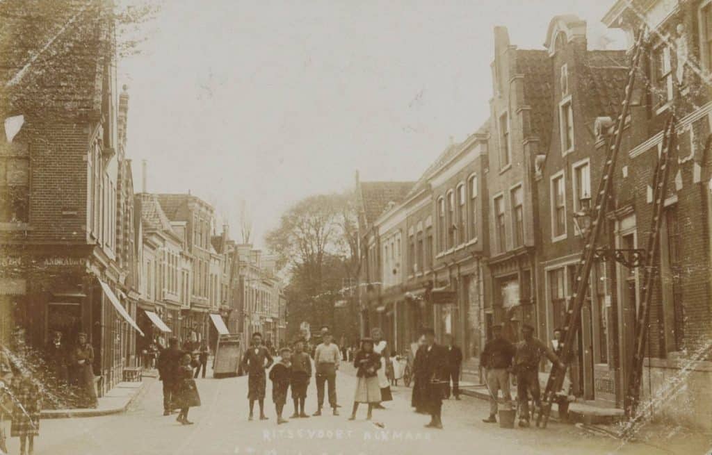 Prentbriefkaart Links Ritsevoort 1, de wijnkoperij van Andrau & Co. Rechts Ritsevoort 2, het Hofje van Splinter. Twee ladders, waarschijnlijk van glazenwassers, staan tegen de voorgevel. Een aantal mensen poseert voor de fotograaf. Foto P Jonker circa 1904.