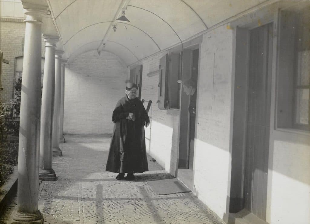 Een vrouw loopt door de galerij van het Hofje van Splinter. Circa 1930. Foto Houwer-van Agtmaal.