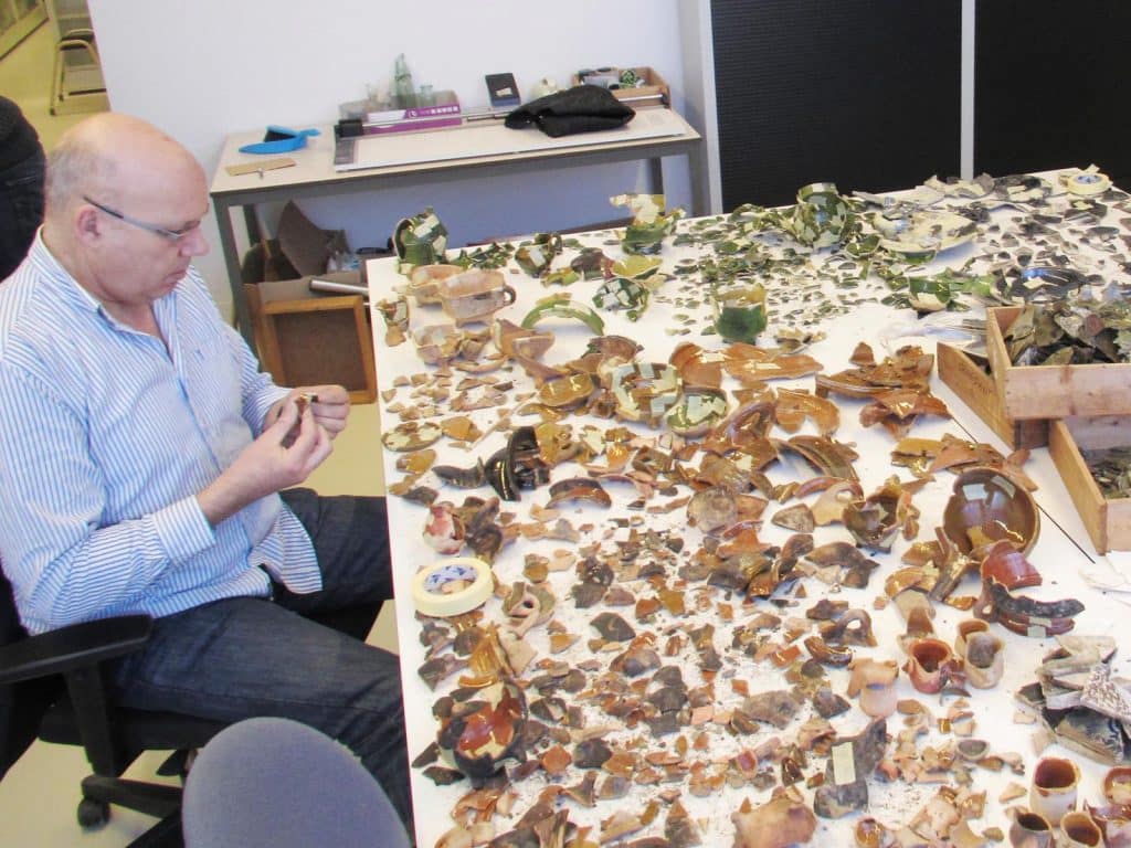 Op werktafels worden de scherven uit een beerput gesorteerd, gepuzzeld en geïnventariseerd door Rob Roedema. 2013.