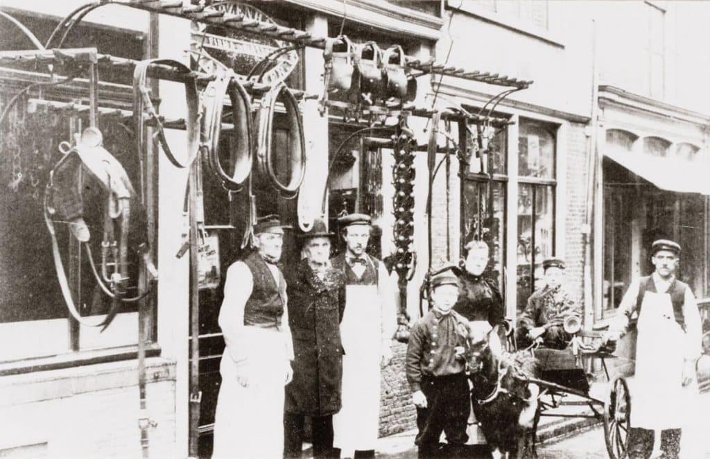 Zadelmakerij van Rozenhart gevestigd aan Achterdam 1 sinds 1794. Foto uit 1898. Derde van links grootvader Rozenhart en bij de bokkewagen grootmoeder Rozenhart. Op de bokkewagen J. Rozenhart, de vader van A.F. Rozenhart die het laatst in de zadelmakerij heeft gewerkt.