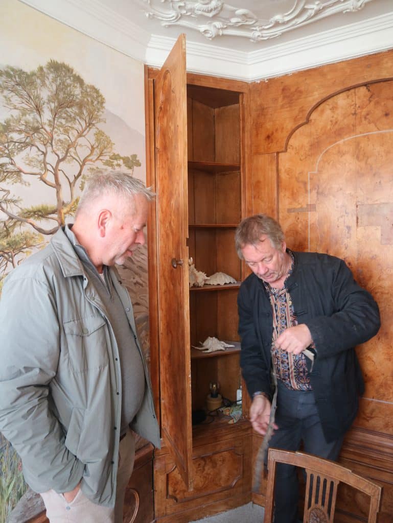Rob de Vries laat een reepje canvas zien dat ze gevonden hadden op de muren van de erkerkamer van het Smalste Huisje