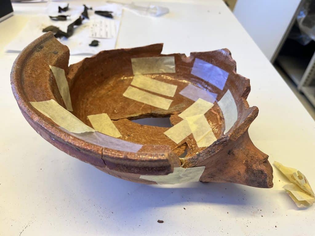 Lage kookpot op drie pootjes. Wrakgoed met sterk bekrast glazuur door veelvuldig gebruik. Datering: circa 1650-1680.
