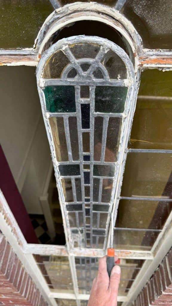 Restauratiewerk aan de buitenkant van het glas-in-loodraam van onderwijzerswoning aan de Munnikenweg.