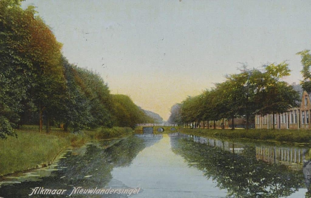 Prentbriefkaart van de Popmansbrug over de Nieuwlandersingel uit circa 1925. De Popmansbrug over de Nieuwlandersingel (voorgrond) en de Baansingel, die het Klein Nieuwland met het Overdiepad verbond. Links het park op het Kwerenbolwerk, de voormalige stadswal naast het voormalige Kwerenbolwerk, onderdeel van de Vest. Rond 1400 had hier al een brug gelegen. In 1575, vlak na het beleg van Alkmaar (1573) tijdens de 80-jarige oorlog, werd besloten de brug "opnieuw aan te leggen". Het werd vermoedelijk een ophaalbrug. In 1597 werd dat zo aangegeven, net als in 1818. Het werd de Nieuwlanderpoortbrugge genoemd. Erachter lag de Nieuwlanderpoort, naast het Kwerenbolwerk. Rond 1898 werd er daar een kneppelbrug (knuppelbrug) gelegd. In de twintiger jaren werd de naam veranderd in Popmansbrug, naar de heer Popman uit de 17e eeuw. Na de restauratie rond 1977 werd het helemaal een stenen brug. Ingekleurde foto.