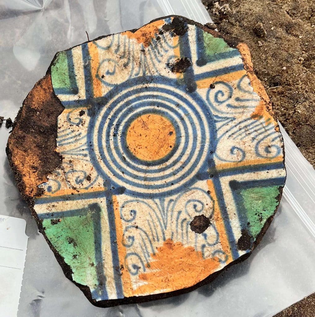 Bodemfragment van een majolica schotel met een meerkleurige versiering. We zien een kruis, ingevuld met versieringen die mede ontleend zijn aan importaardewerk uit Italië (ca. 1575-1625).