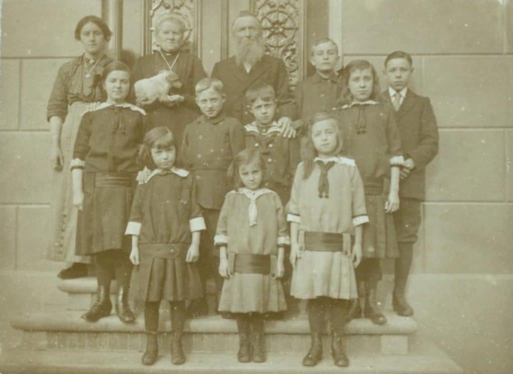 Groepsfoto Doopsgezinde weeshuis aan de Tuingracht in De Rijp. Het zijn Belgische kinderen die hier werden opgevangen. Op de achterste rij, de tweede en derde van links, de binnenmoeder en -vader van het Weeshuis. De groep staat bij de achter-ingang van het voormalige Doopsgezinde weeshuis aan de Tuingracht in de Rijp. 1914.