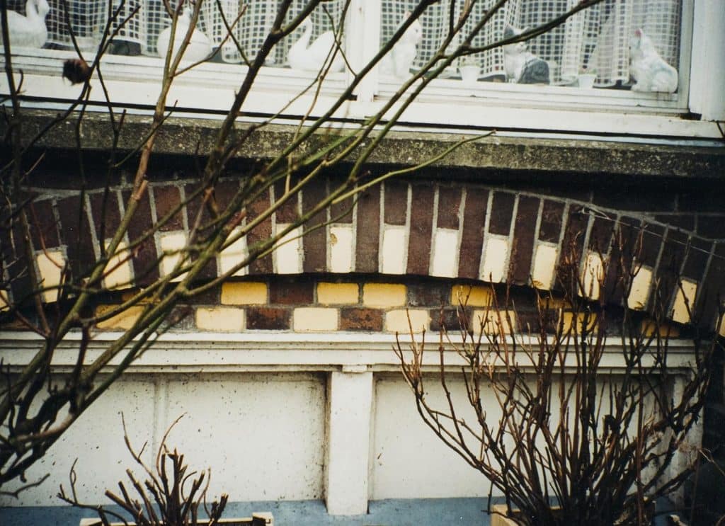 Boven het raam zit een sierlijke segmentboog met gekleurde accenten. Circa 2002