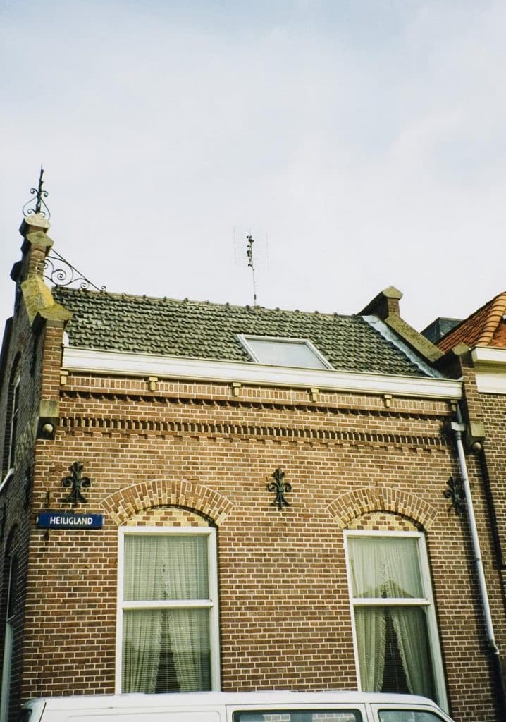 De Brugwachterswoning aan de Eilandswal. Boven de ramen zitten sierlijke segmentbogen met gekleurde accenten en subtiele details. Zoals kleine loodslabjes die als een soort ‘opgerolde randjes’ zijn vormgegeven. De houten goten met hun getrapte kroonlijst en de sierlijke gootklossen maken het geheel af. Foto A. Schoots 2002.