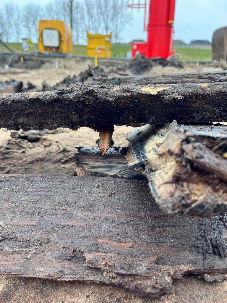 Goed bewaarde eikenhouten delen van een ingegraven goot uit de opgraving aan de Westdijk 21c. Op de achtergrond de motorpomp en filter van de bronbemaling.