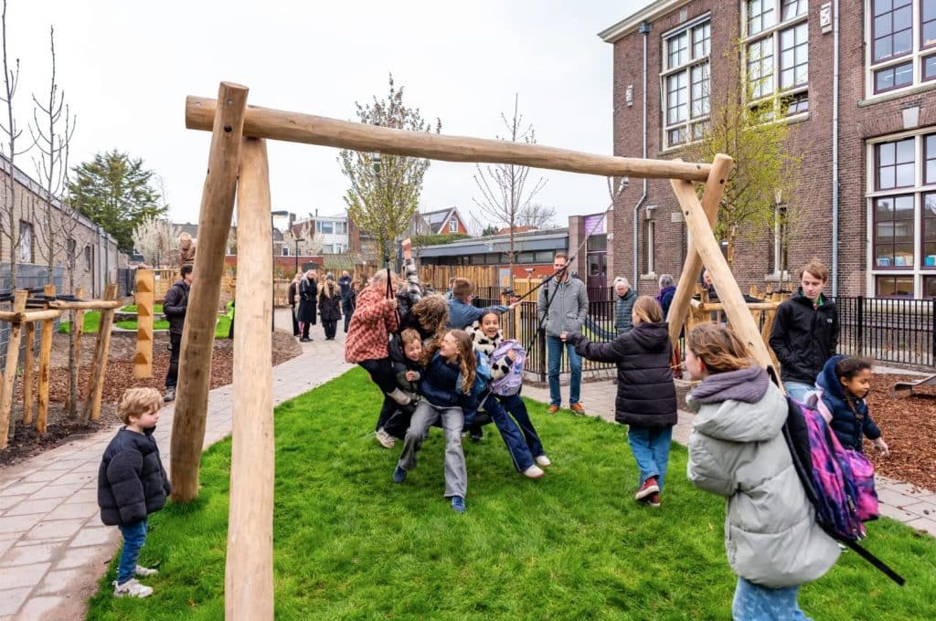 Blije kindere op een grote schommel op het vernieuwde schoolplein van Bello.