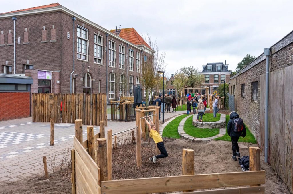 Kinderen spelen op de nieuwe speeltoestellen. Links de gevel van basisschool Bello.