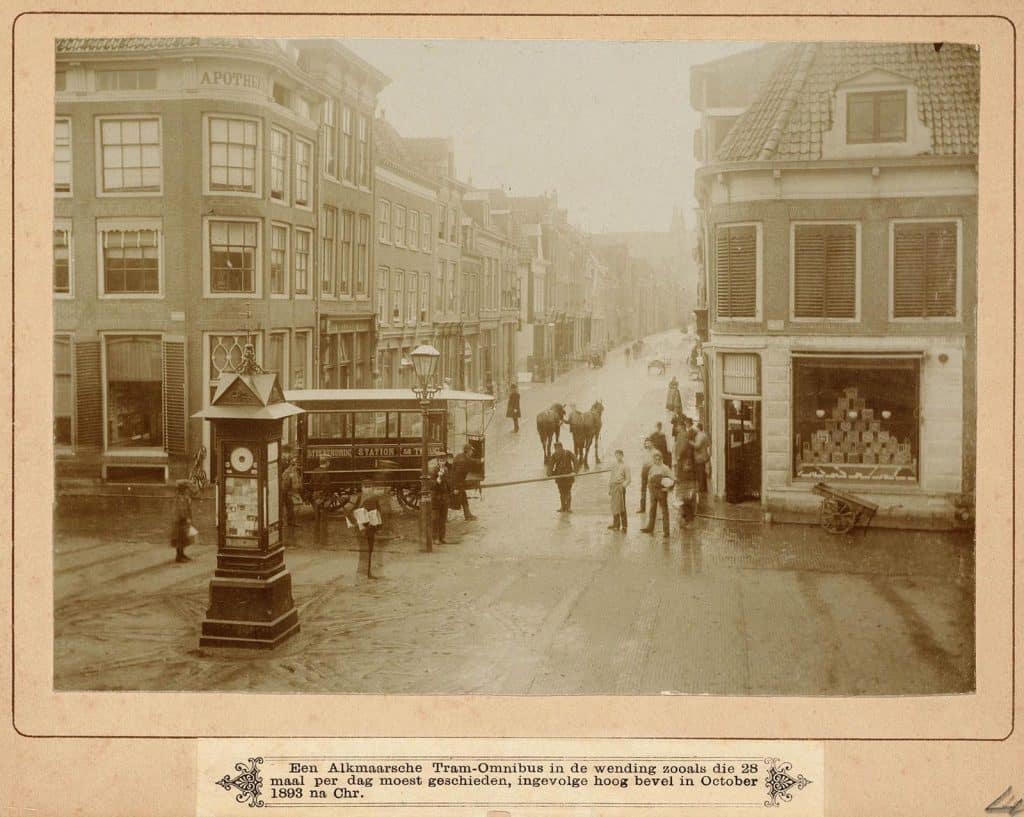 Links staat een paardentram. Er lopen een aantal mensen op straat.