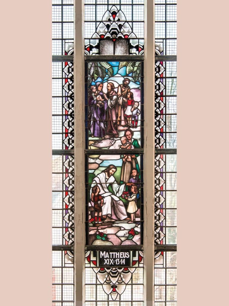 Gebrandschilderd raam met een voorstelling uit het Nieuwe Testament. De mensen brachten hun kinderen bij Jezus. Zij wilden graag dat Hij zijn handen op hen zou leggen en voor hen zou bidden. Jezus zegent de kinderen.