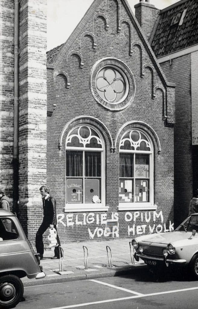 Op de onderkant van de pui is 'religie is opium voor het volk' geschilderd met witte druipende letters.
