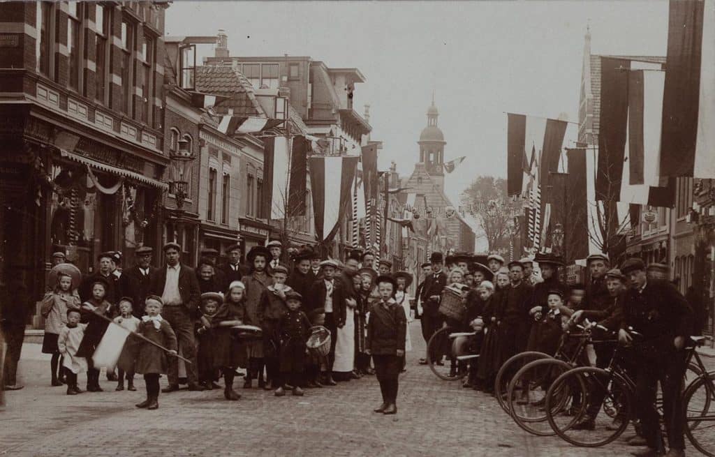 De Laat ter hoogte van de Ridderstraat in 1909. Vlaggen en mensen op straat ter ere van de geboorte van Prinses Juliana. In de achtergrond de Kapelkerk.