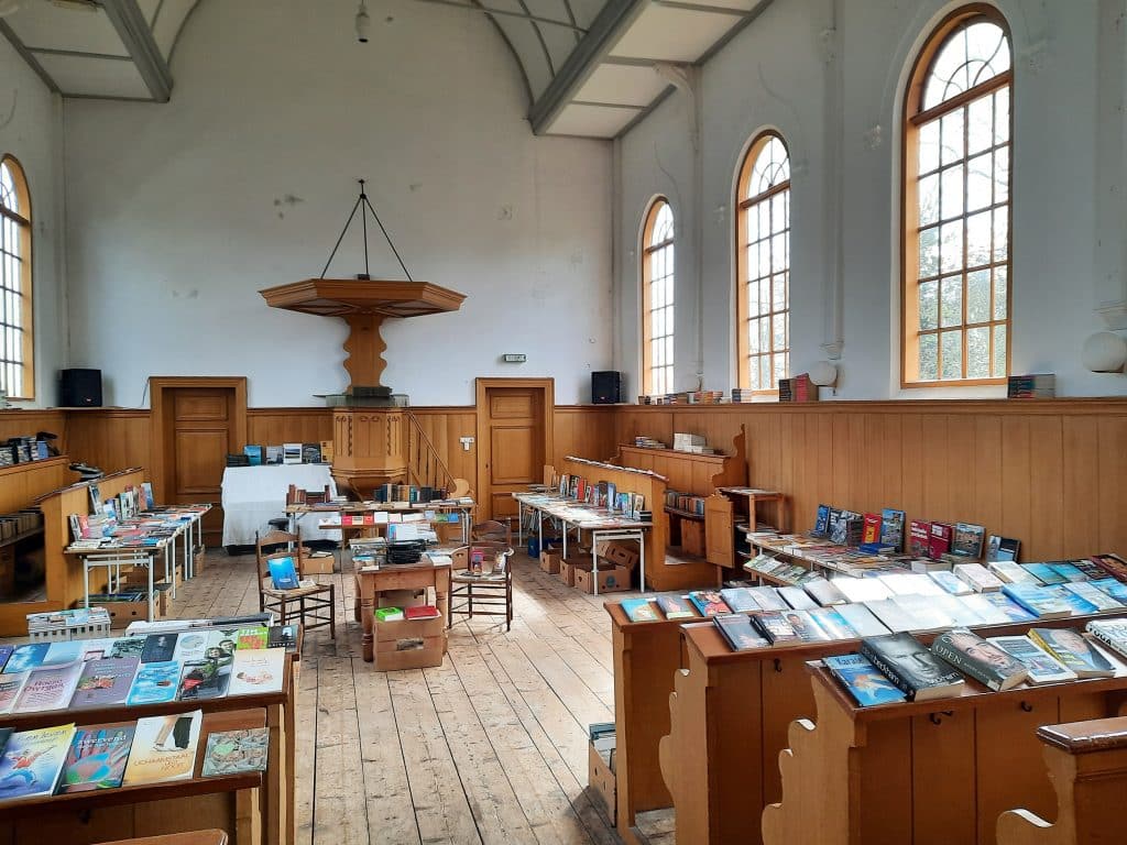 Op de kerkbanken liggen boeken die verkocht worden. Je kijkt richting de oude preekstoel.