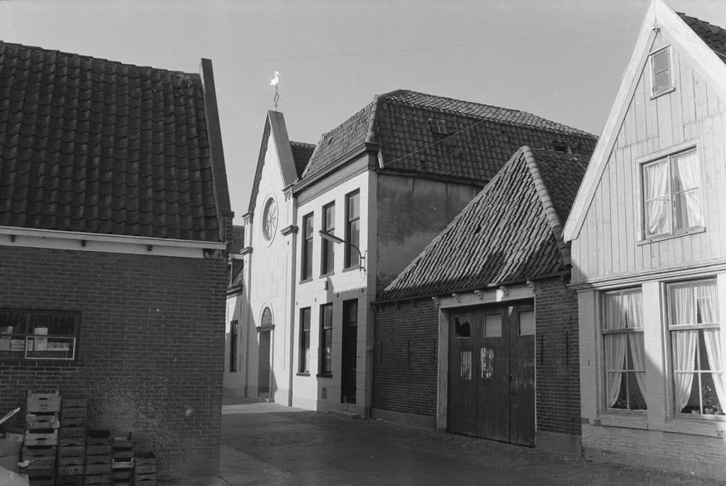 Links een zijmuur van Rechtestraat 1. Er staan groentekisten tegen de muur.