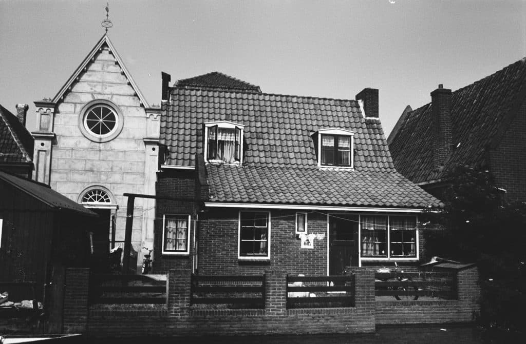 Opname over het water van de Tuingracht. Aan de overkant van de Rechtestraat de voormalige Lutherse kerk, nu De Groene Zwaan. Twee spelende kinderen in een badje. Waslijn, was, bromfiets.
