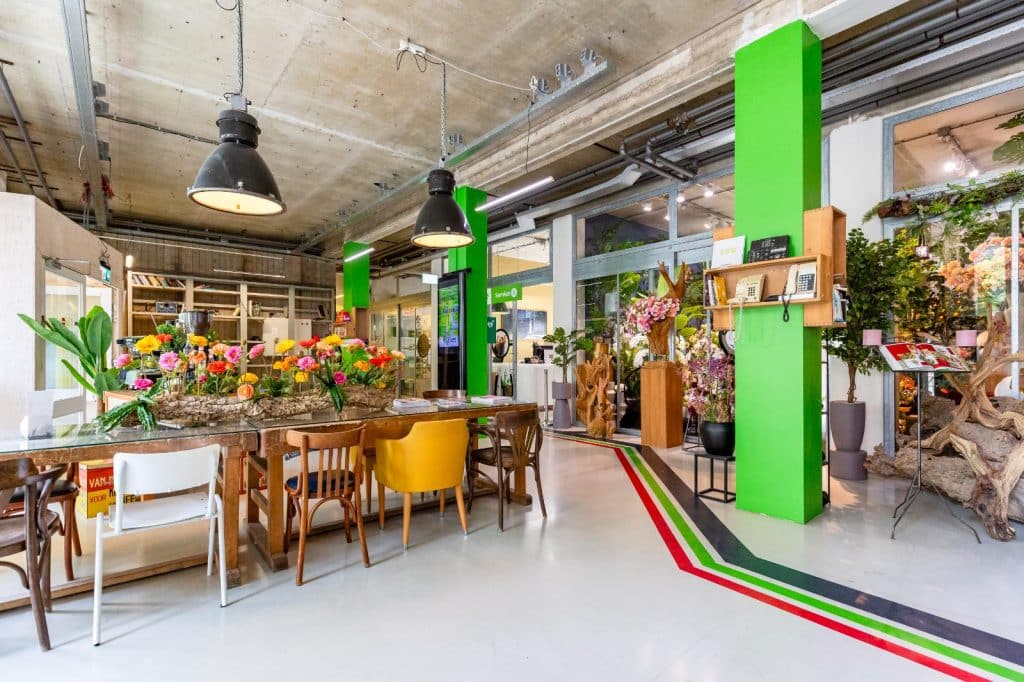 Er staan bloemen op de eettafel waaromheen allemaal verschillende eetstoelen staan. De pilaren zijn groen.
