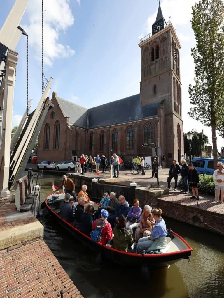 De ophaalbrug voor de kerk staat open en er vaart een boot vol met mensen de sluis in richting Graft.